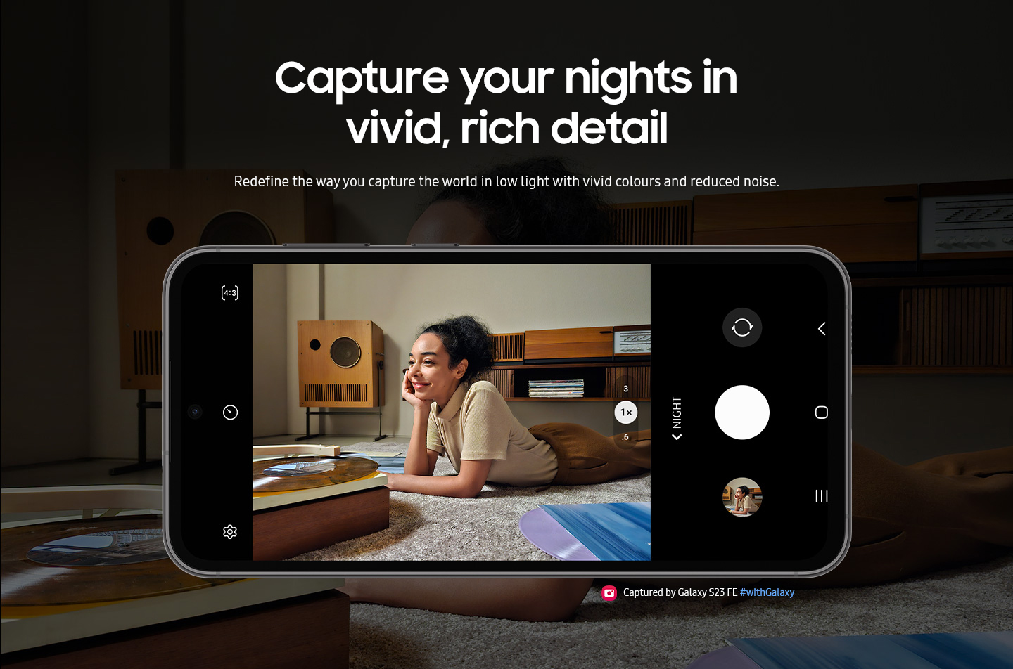 A Galaxy S23 FE device seen from the front and horizontal. The screen in picture mode shows a clear image of a woman listening to vinyl against the backdrop of a dimmer light setting. Text reads Captured by Galaxy S23 FE #withGalaxy.
