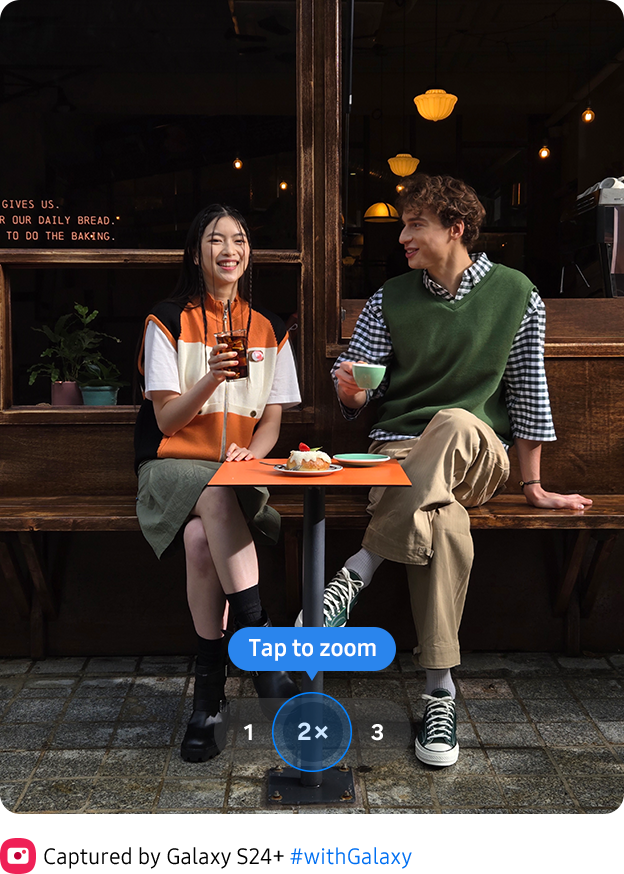 A colour rich photo of two people sitting in front of a cafe taken at 2x zoom.