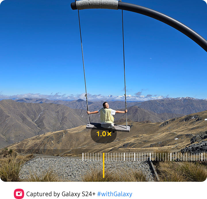 ai zoom. The view finder of the Camera app shows a woman posing in front of a scenic background. 