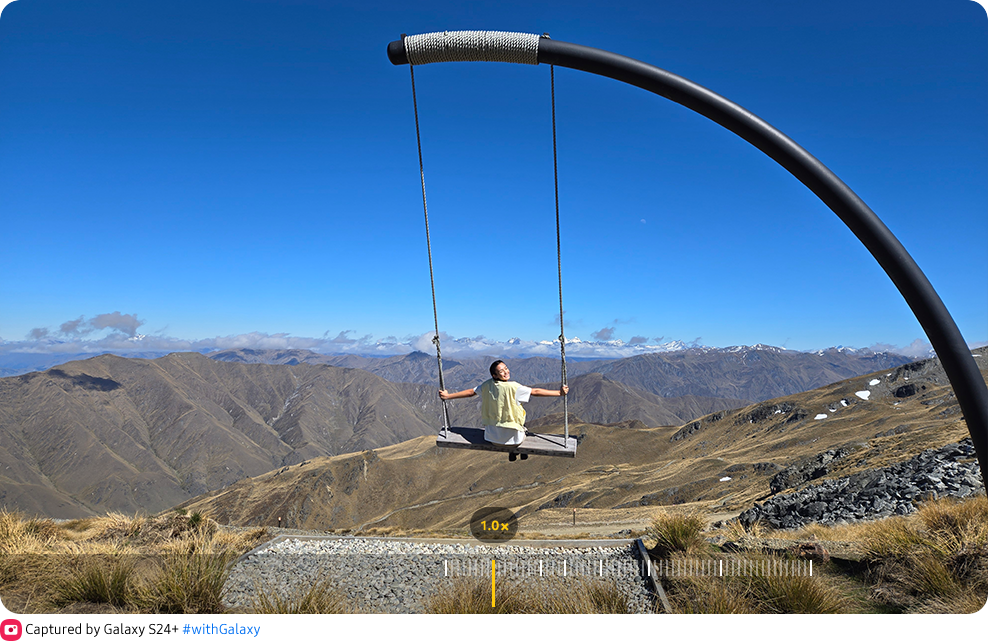 ai zoom. The view finder of the Camera app shows a woman posing in front of a scenic background. 